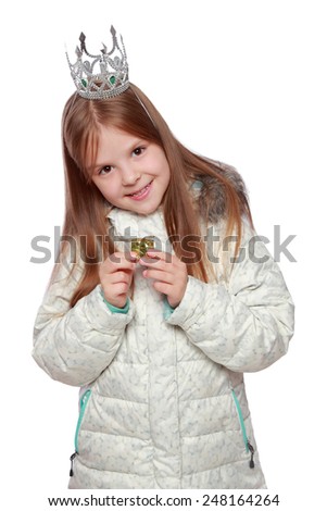 Studio image of a cute cheerful little girl in a warm white coat with a crown on his head holding a small gift isolated on white on Holiday