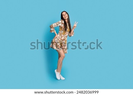 Full length photo of shiny attractive lady dressed floral print outfit showing v-sign empty space isolated blue color background