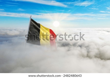 Belgium flag aerial view in beautiful sky with clouds. Top-down drone shot at sunrise or sunset. Aerial bird's eye view of the flag with cloudscape.