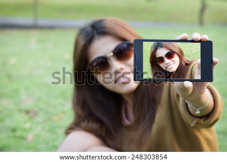 pretty women wear eyeglass smile use smart phone mobile take self picture selfie in park
