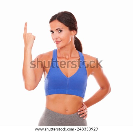 Isolated sporty brunette female wearing shorts pointing up on isolated background - copyspace
