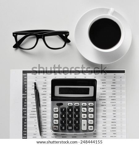 high-angle shot of a desk with a calculator, a pen, a balance sheet, eyeglasses and a cup of coffee in an office