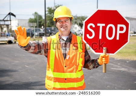 Friendly construction worker in the road holding up a stop sign.  