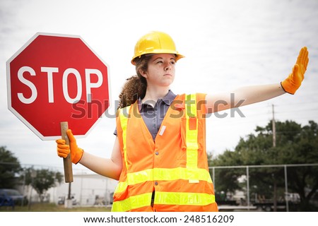 Female construction apprentice holding a stop sign and directing traffic.  