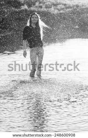 Beautiful girl with long, straight hair posing and playing with water in a small river. Black and white, artistic photography 