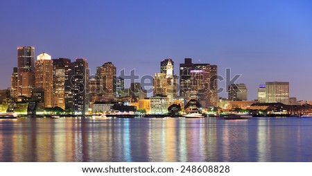 Boston downtown skyline panorama with skyscrapers over water with reflections at dusk illuminated with lights. 
