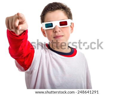 Caucasian smooth-skinned boy wears a pair of 3D Cinema paper googles with red and sky-blue lenses and looking calm and confident points to viewer with right hand