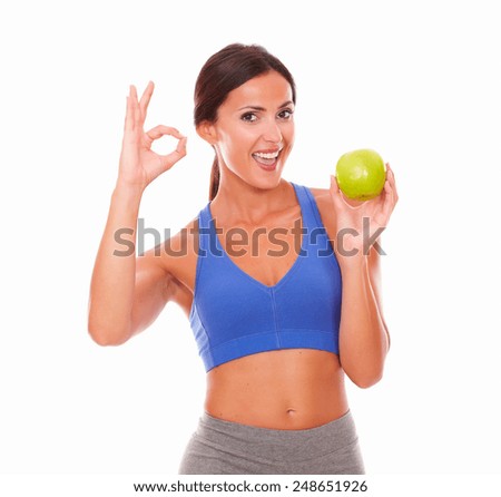 Pretty latin woman in exercising outfit holding fruit with the left hand on isolated background