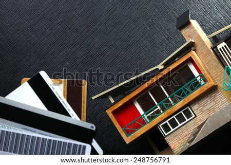 Vintage and old plastic house model put on the black color leather background represent the house mortgage related in the scene appear the credit cards out of focus as a background.