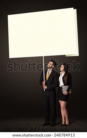 Young business couple holding a big, white post-it paper 