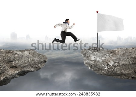 Man jumping on cliff with blank white flag and gray cloudy cityscape background