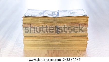 Thick stack of US cash. The stack of US cash in mixed notes of different colors and tones, positioned on the wooden table