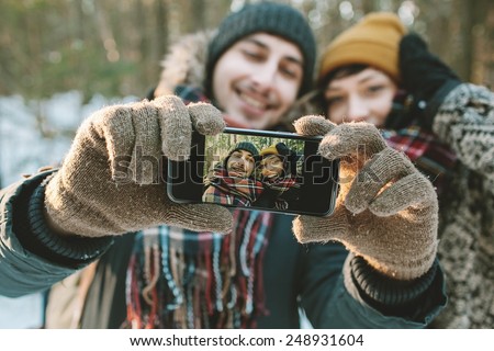 Young hipster couple taking selfie in winter forest with smartphone