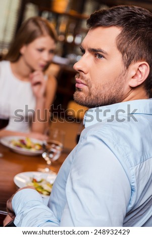 Relationship difficulties. Frustrated young man looking away while sitting together with his girlfriend in restaurant 
