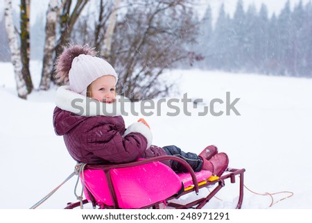 Adorable little happy girl sledding in winter snowy day