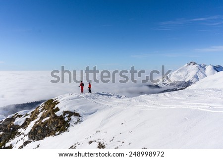 Two skiers standing on top of a mountain above the clouds