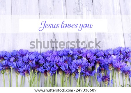 Beautiful cornflowers and text Jesus loves you on wooden background