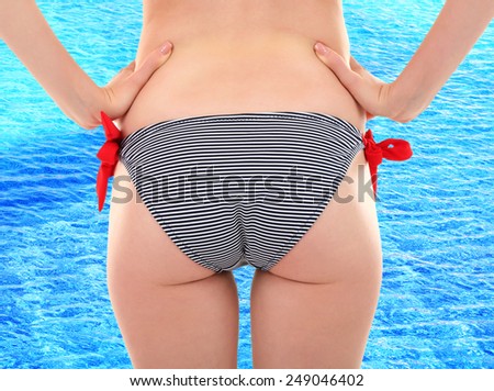 Young woman with slim body in swimsuit on swimming pool water background