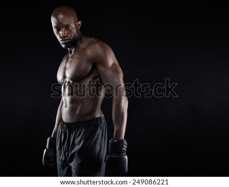 Portrait of muscular male boxer with boxing gloves against black background. Professional boxer looking at camera.