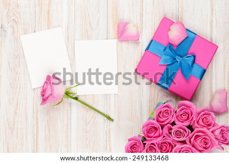Valentines day background with gift box full of pink roses and two blank photo frames over wooden table. Top view with copy space