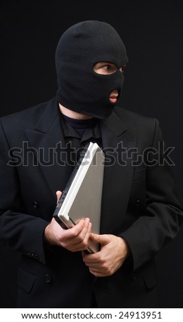 A business thief wearing a black balaclava is stealing a laptop computer