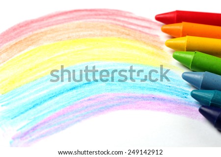 Crayons lying on a paper with children's drawing rainbow. Selective focus, copy space background