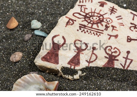 stone with petroglyphs on the sand, surrounded by sea shells