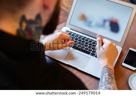 Tattoed man with beard work with laptop during a lunch.