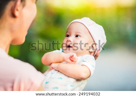 a romantic soft focus picture of 3 months baby feeling happy and smiles with her mother in the morning sunlight. Portrait of Asian family.
