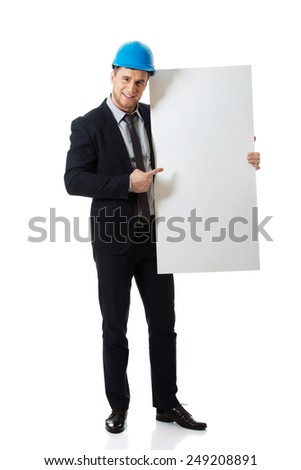 Handsome businessman in hard hat pointing on empty banner.