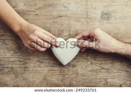 Hands of man and woman connected through a white heart. Studio shot on a wooden background, view from above.