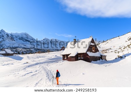 Backpacker in front of wooden mountain hut in winter landscape of Gasienicowa valley, Tatra Mountains, Poland