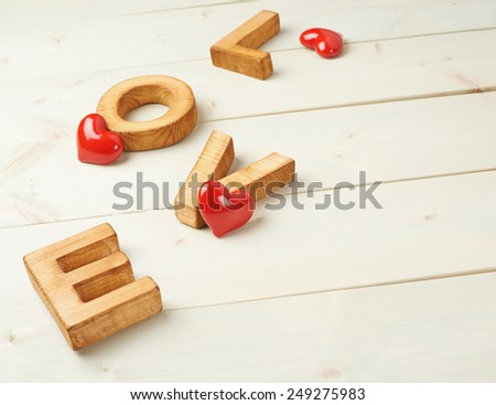 Word Love made with block letters over the wooden surface next to few glossy red hearts as a Valentine's Day love composition, background