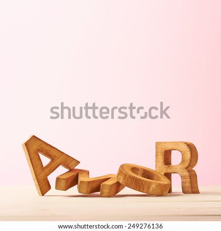 Word Amor meaning Love in multiple languages as a composition of wooden block letters against the pink background