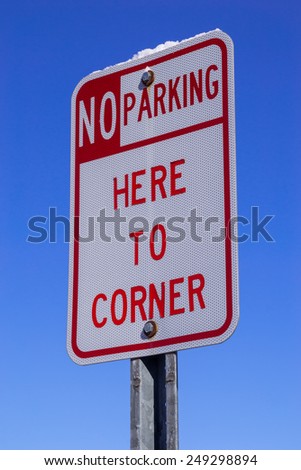 The "No Parking here to corner" sign with blue sky background.
