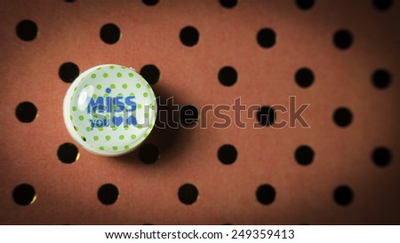 Round cute thumbtack or pushpin for whiteboard, notice board, gift card or special occasions with Miss You message on polka dot vintage patterns background. Slightly defocused and close-up shot