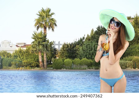 Young woman in swimsuit with cocktail on swimming pool background