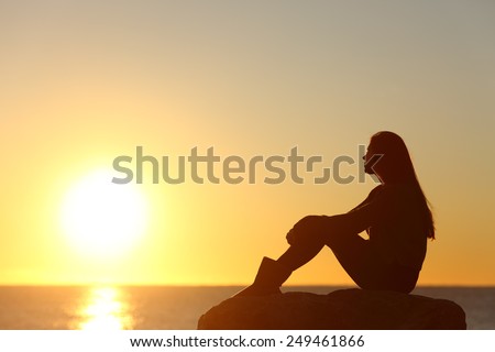 Profile of a woman silhouette watching sun on the beach at sunset Royalty-Free Stock Photo #249461866