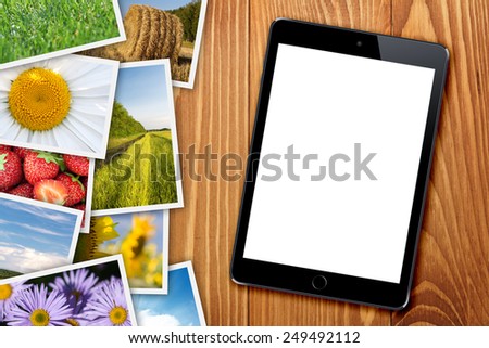 Tablet with blank screen and stack of printed pictures collage on wooden table