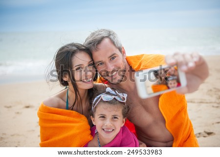 A young couple and their daughter are taking a selfie at the beach. Focus on the screen of the phone