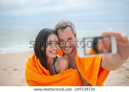 A young couple is taking a selfie at the beach. Focus on the couple