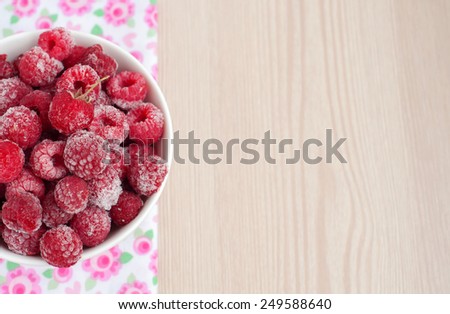 Frozen raspberries in a white bowl on wooden background with free text space. Top view