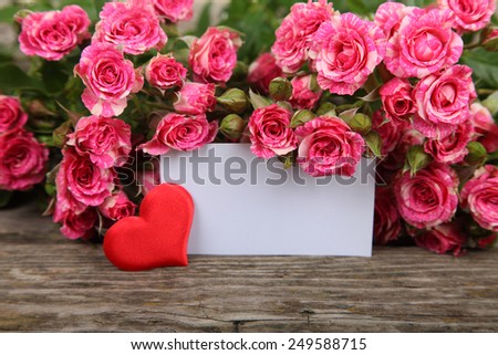 Bouquet of pink roses, heart  and greeting card on a wooden background