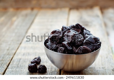 prunes in a bowl on a dark wood background. tinting. selective focus