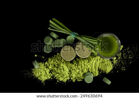 Green food supplements chlorella, spirulina, wheatgrass, pills, powder, tablets, grass blades and green juice isolated on black background, top view. Detox.