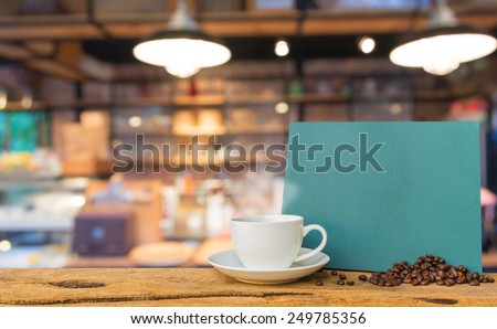 White cup of coffee and green chalkboard menu on wooden bar with Coffee shop blur background with bokeh image .