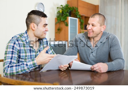 Adult smiling man explains to his friend to fill banking document at home