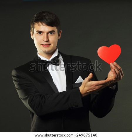 nice handsome man in a tuxedo with a red paper heart. On a black background. vintage toning