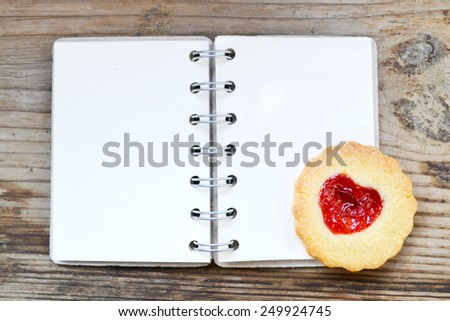 Homemade cookies with heart shaped jam and empty retro spiral recipe book on wooden table