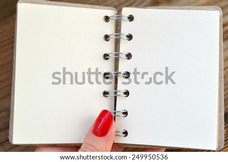 Beautiful woman's hand with red nails holding an empty retro spiral notebook with old paper